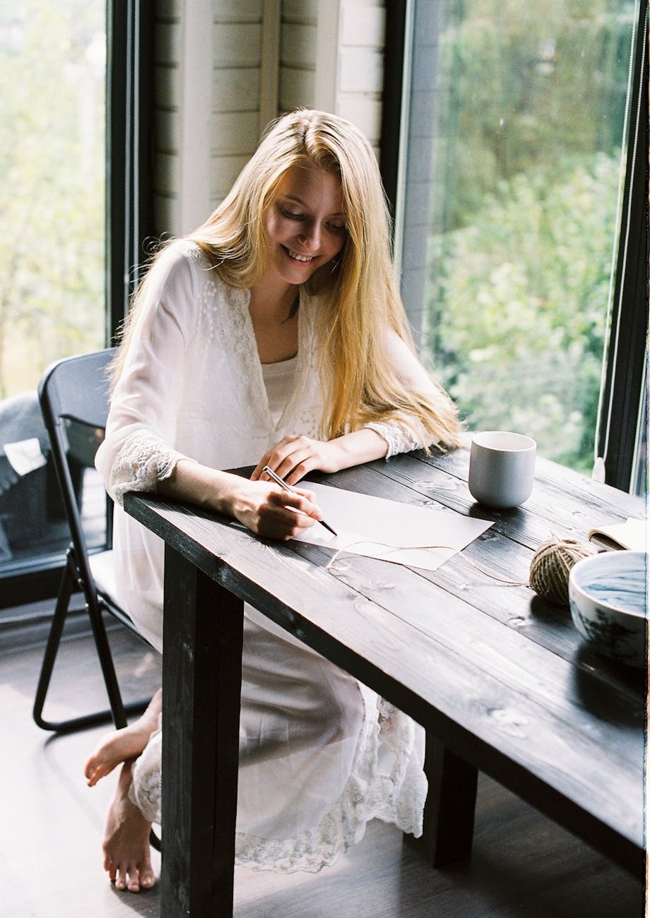 smiling barefooted lady writing thoughts on paper at home