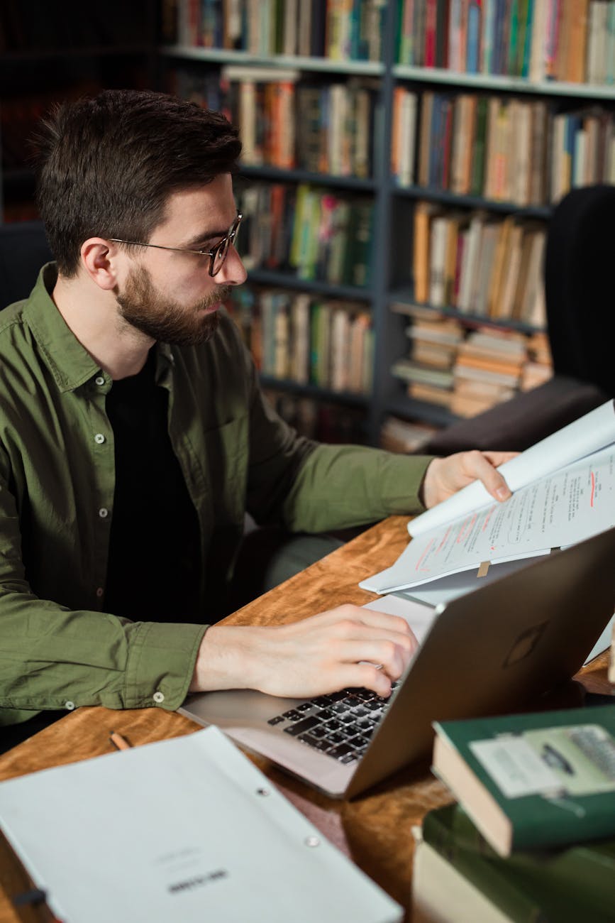 man using a laptop while holding pages